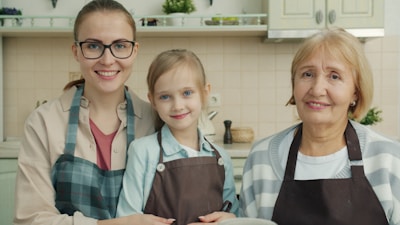 Three smiling women in a kitchen wearing aprons.