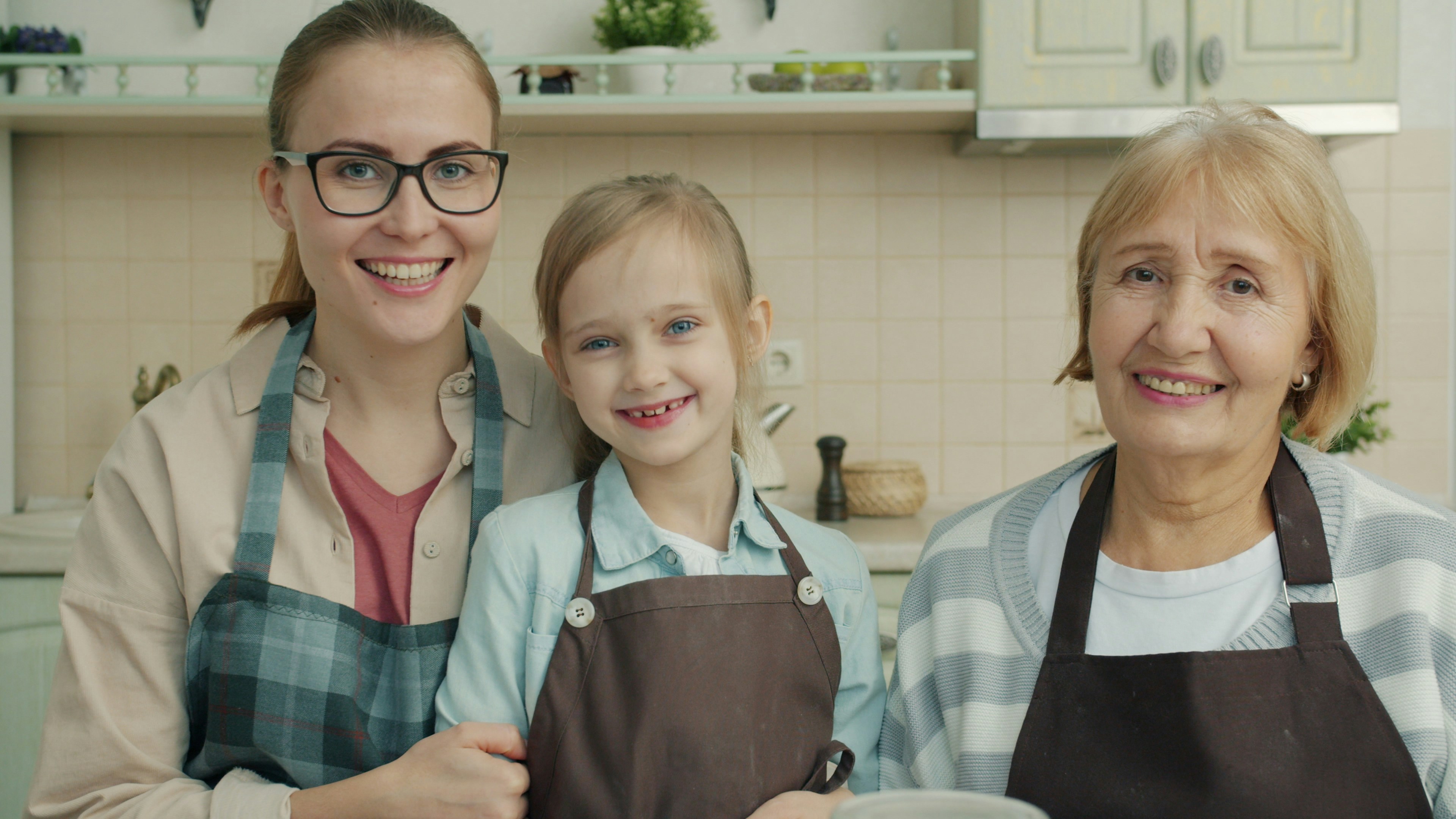 Three smiling women of different generations in aprons.