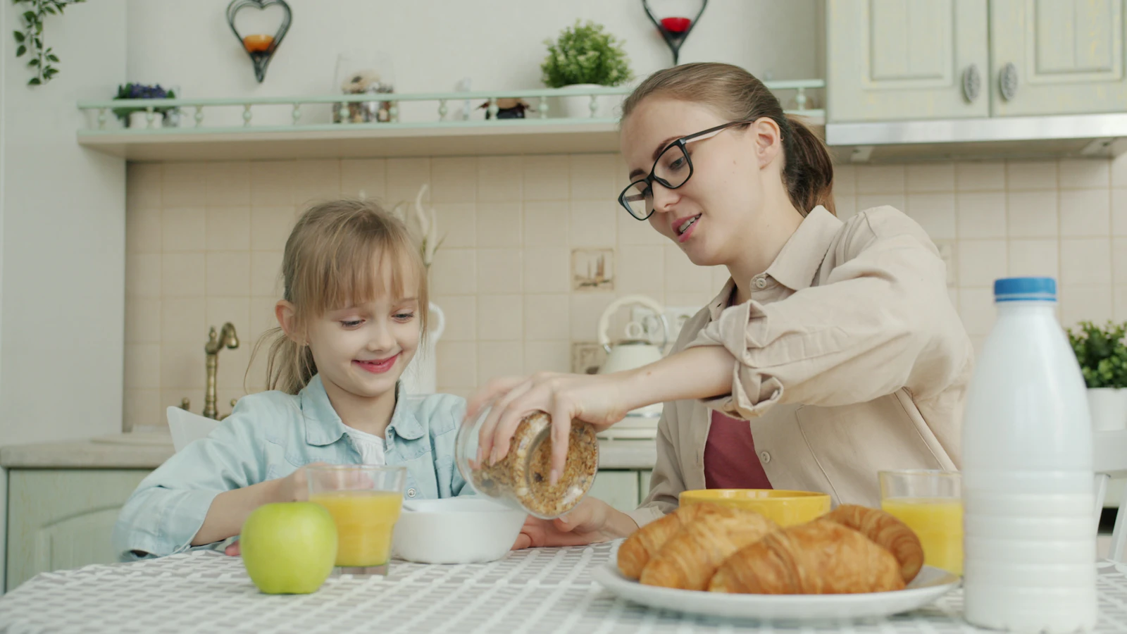 A young woman prepares breakfast while talking with her daughter in a home kitchen