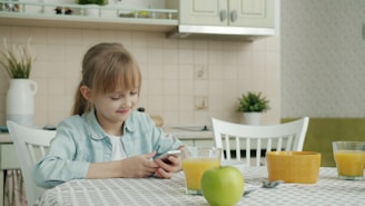 Girl using smartphone at kitchen table with breakfast