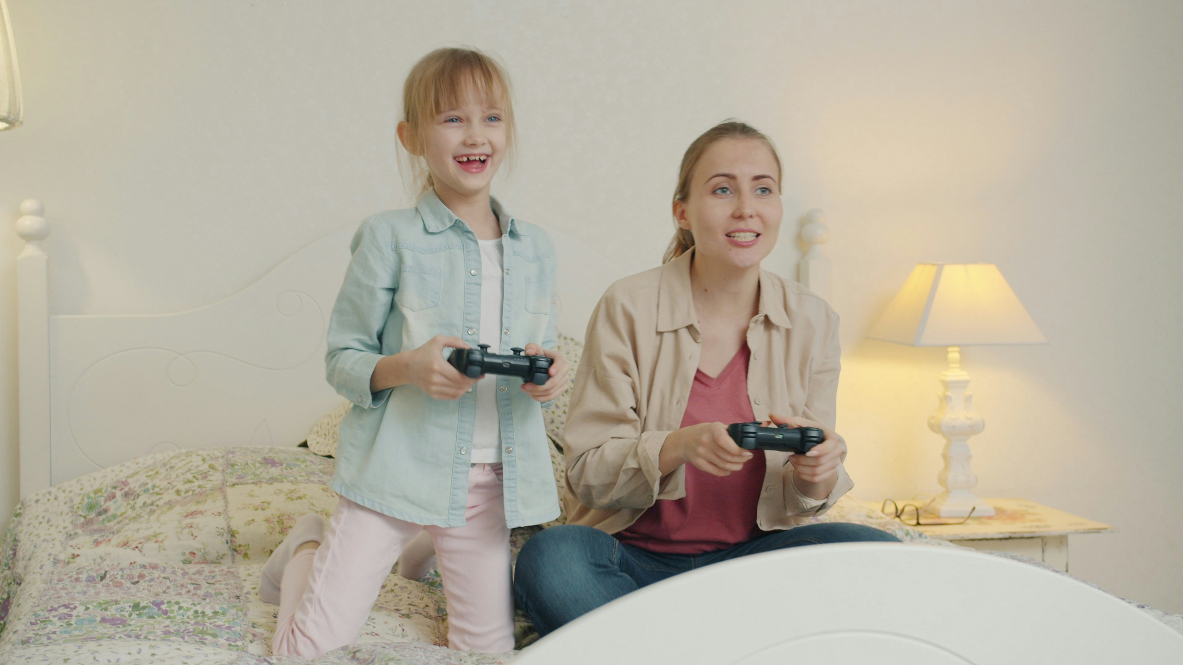 Mother and daughter playing video games together on bed