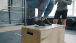 Woman jumping onto a wooden box in a gym.