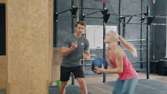 A woman holding a medicine ball with a trainer watching.