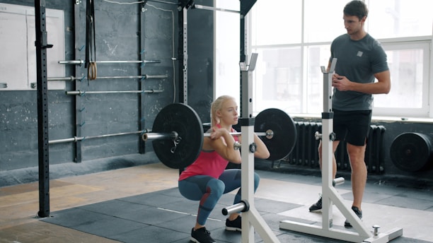 Woman performing barbell squat with trainer watching
