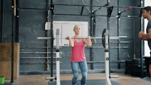 Woman lifting barbell with trainer watching