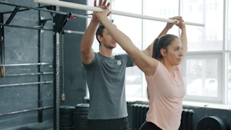 Man assisting woman with barbell exercise in gym.