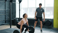 Woman lifting weights with trainer watching