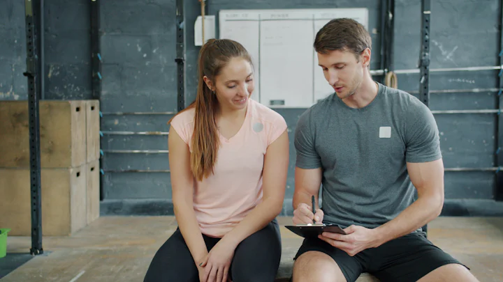 A trainer writing on a clipboard while talking with a gym member