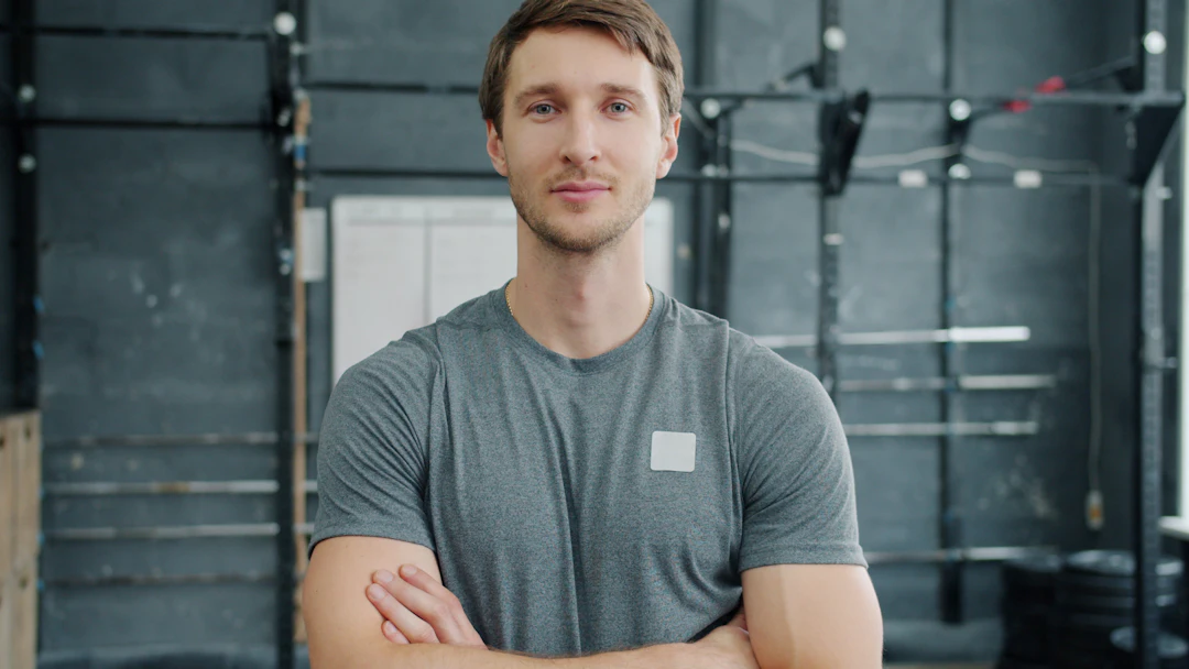 Personal trainer de camiseta cinza e braços cruzados em uma academia