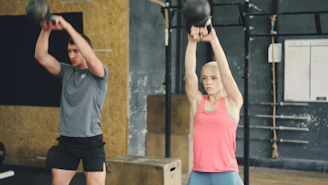 Man and woman performing kettlebell swings in gym.