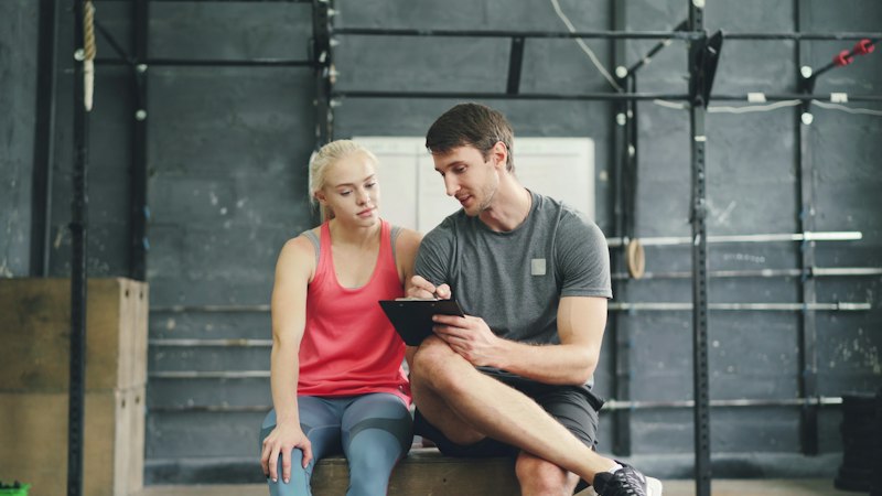 Personal trainer going over a plan on a clipboard with a new client in a gym