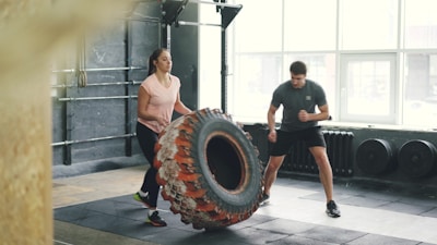 Man and woman flipping tire in gym workout.