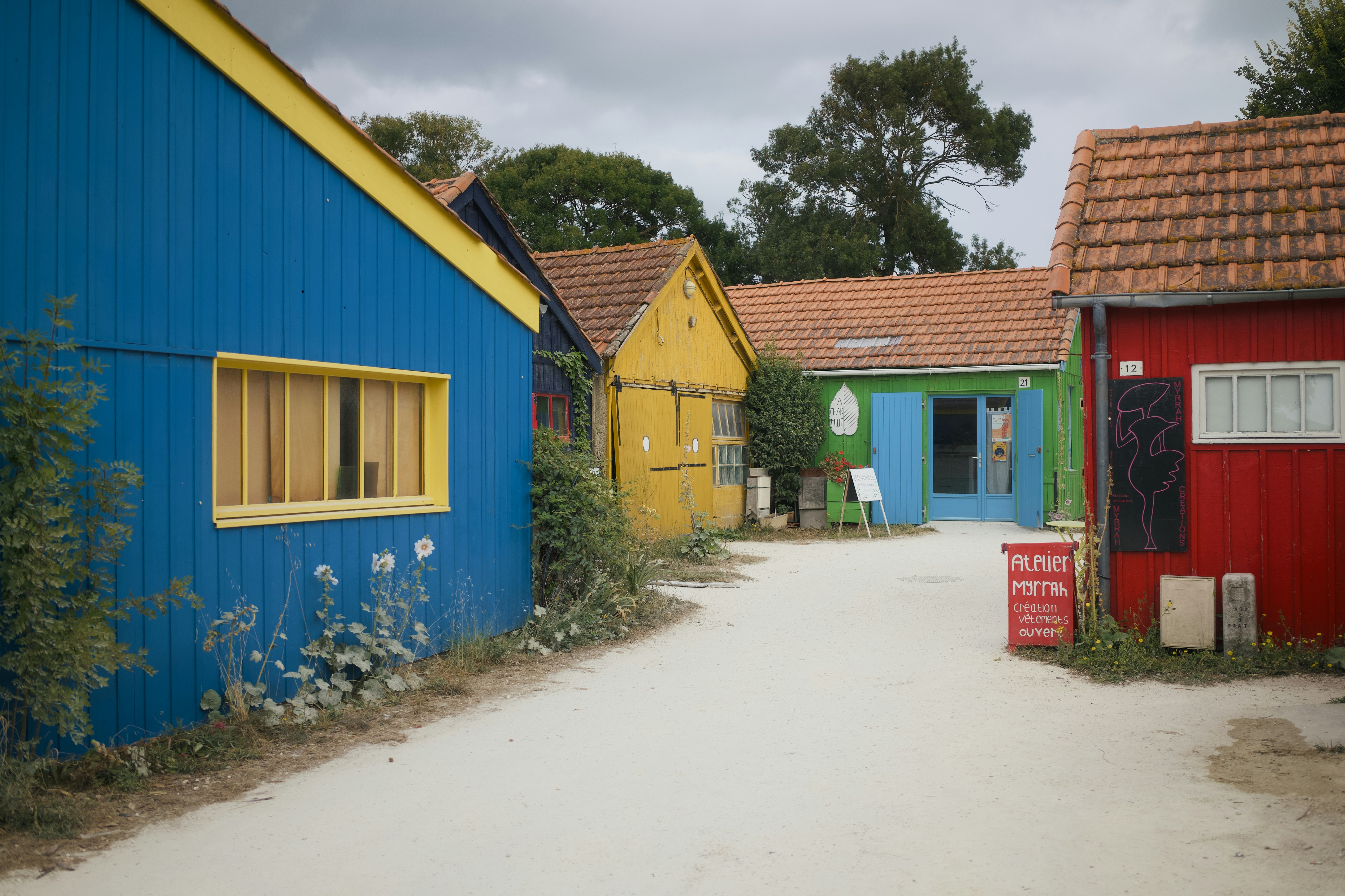 Colorful buildings line a sandy path under a cloudy sky.