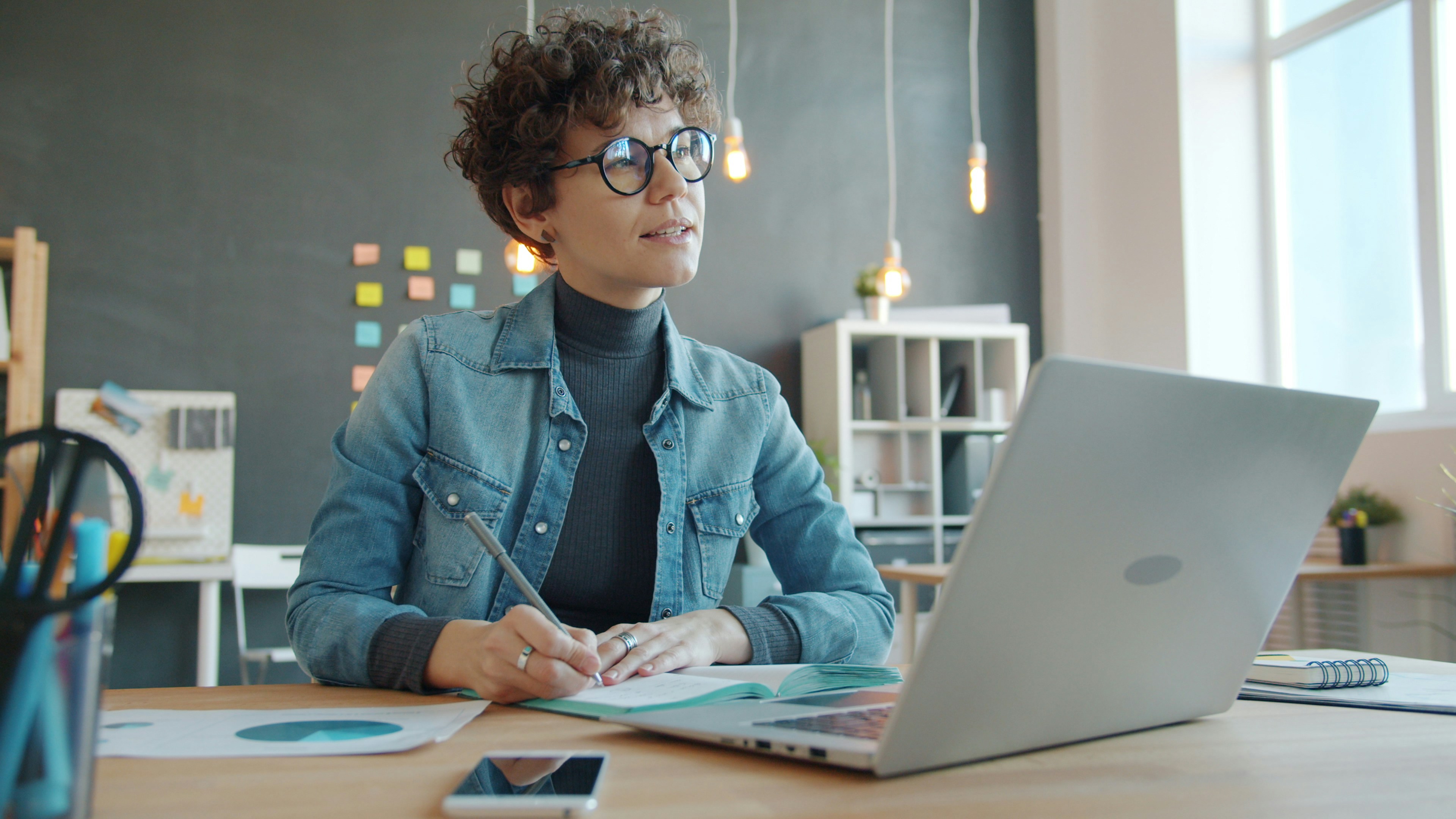 Woman working at a desk with laptop and notebook.