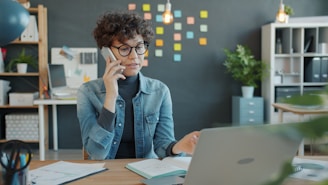 Woman talking on phone at desk with laptop.