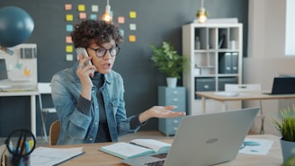 Woman talking on phone at desk with laptop.
