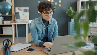 Woman with curly hair working on laptop at desk.