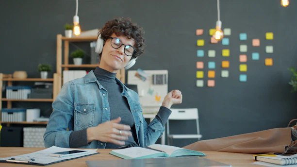 Woman with headphones playing air guitar at desk