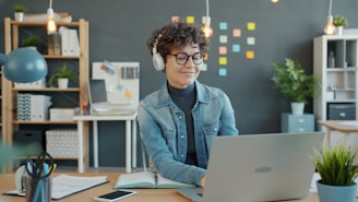 Young woman wearing headphones works on laptop in office.