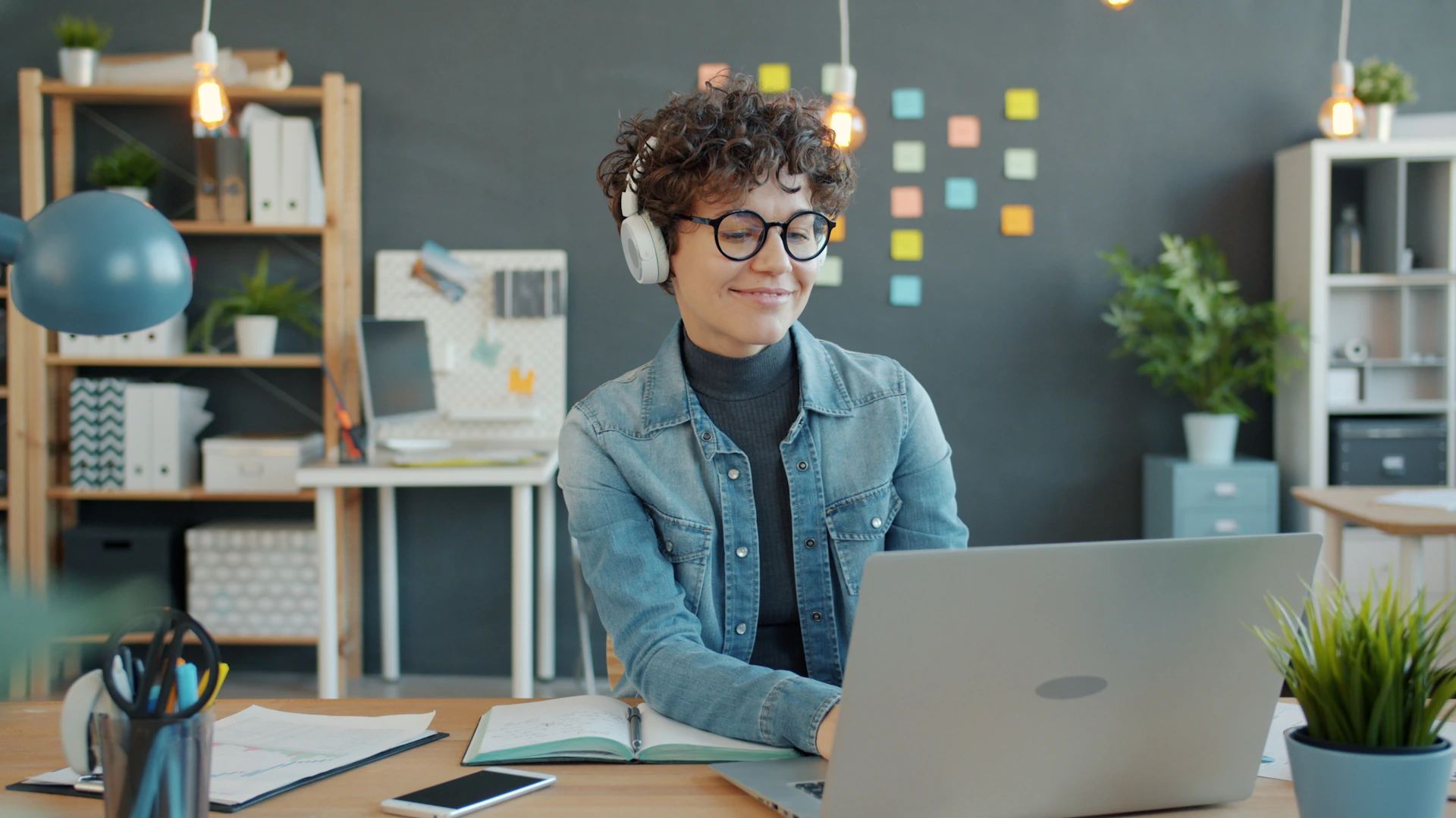 Young woman wearing headphones works on laptop in office