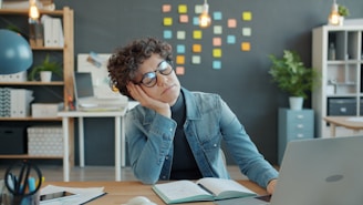 Tired person resting head on hand at desk.