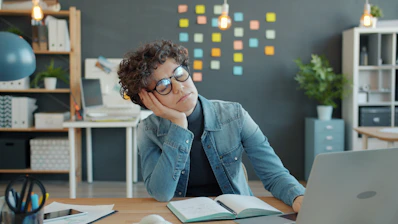 Tired person resting head on hand at desk.
