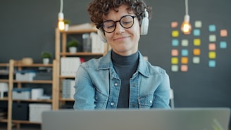 Woman wearing headphones smiles while looking at laptop.