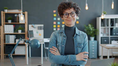 A woman with glasses smiles in an office.