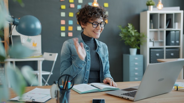Woman waving hello during a video call at desk