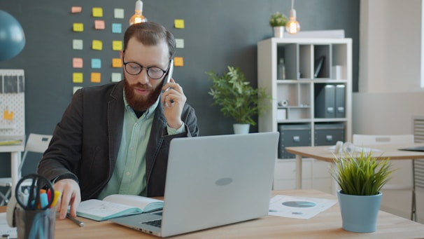 Man in suit talking on phone at office desk.