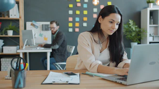 Woman working on laptop in modern office setting.