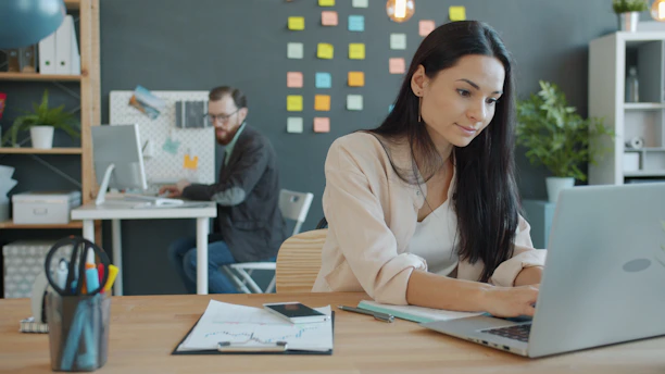 Woman working on laptop in modern office setting.
