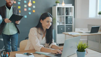 Woman working on laptop with man behind her