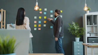 Two people planning with sticky notes on wall.