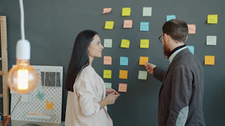 Two colleagues discussing sticky notes on a wall.