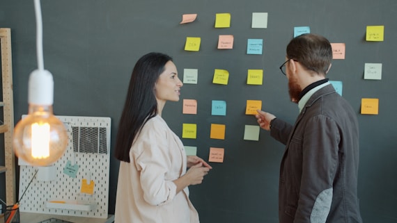 Two colleagues discussing sticky notes on a wall.