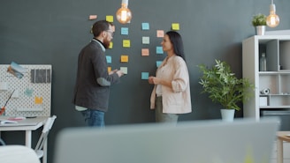Two colleagues brainstorming with sticky notes on wall.