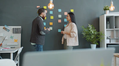 Two colleagues brainstorming with sticky notes on wall.