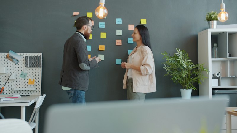 Two colleagues brainstorming with sticky notes on wall