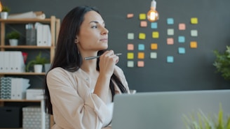 A woman thinking with a pen at her desk.