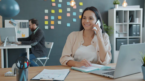 Woman talking on the phone at a desk with a laptop