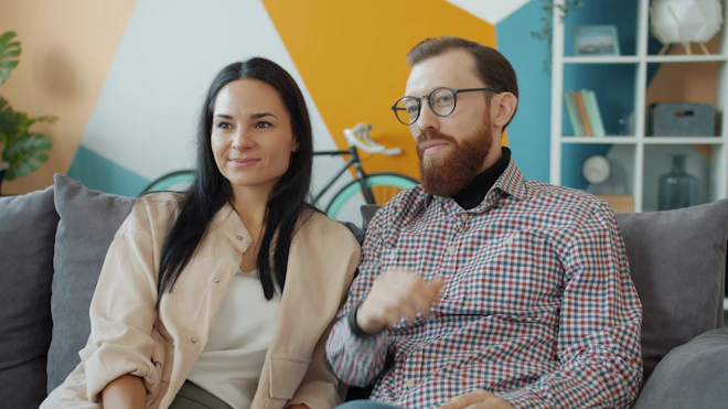 Couple sitting on a couch watching something.