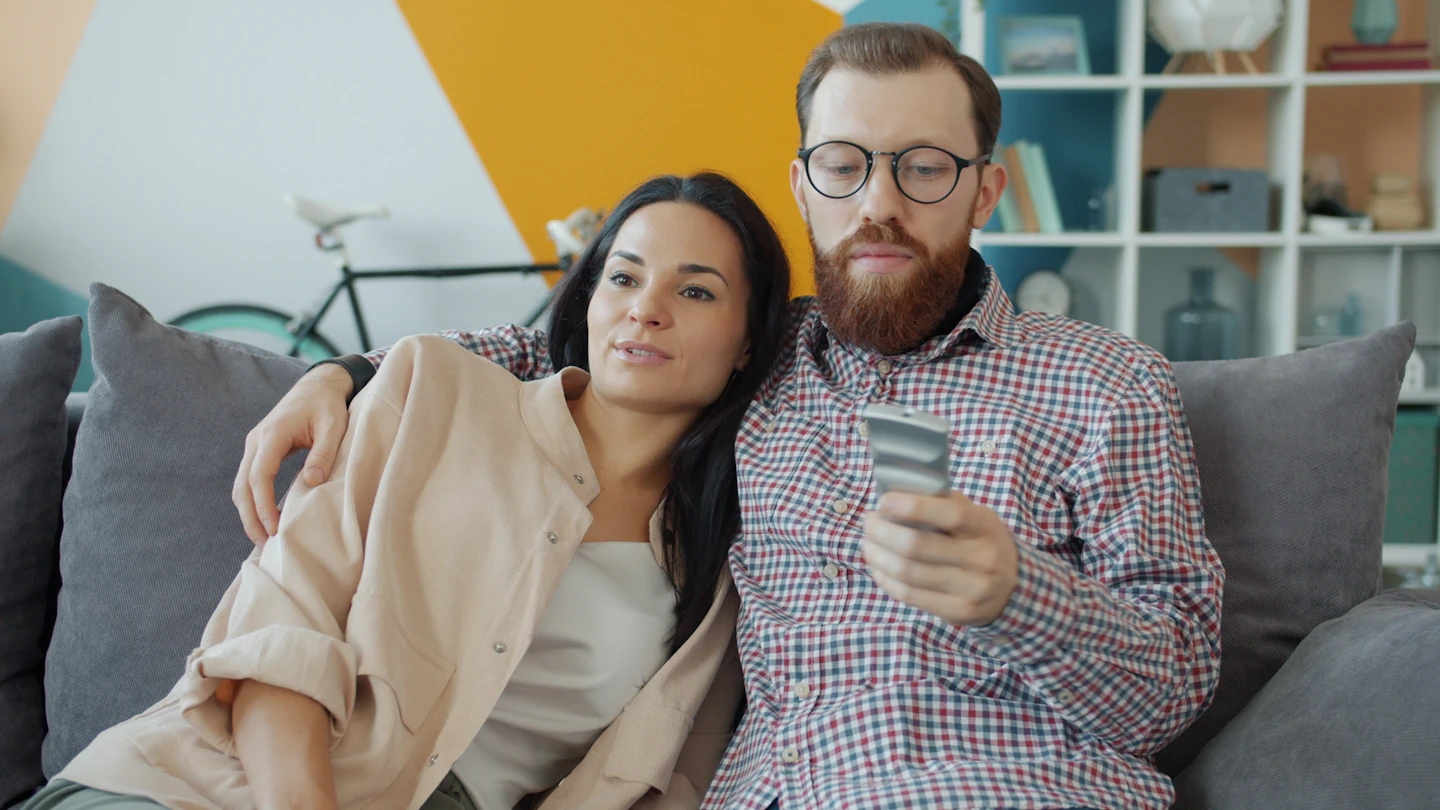 A couple on the sofa choosing what to watch with the remote