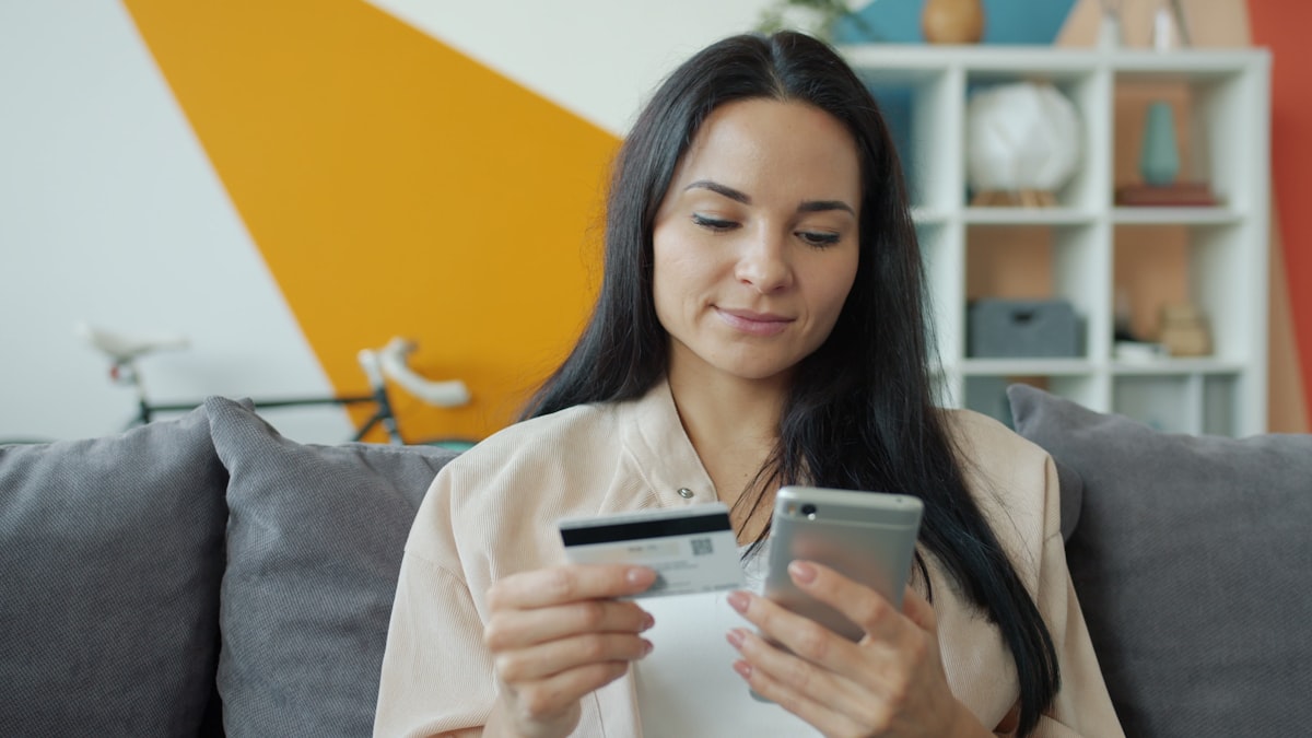 Woman holding a credit card and smartphone while shopping online, representing the buy now pay later consumer finance model at the heart of Klarna's business