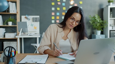 Woman working at a desk with laptop and notebook.