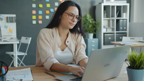 Woman working on laptop in modern office setting.