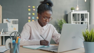 Woman working at a desk with laptop and notebook.