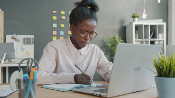 Woman working at a desk with laptop and notebook.