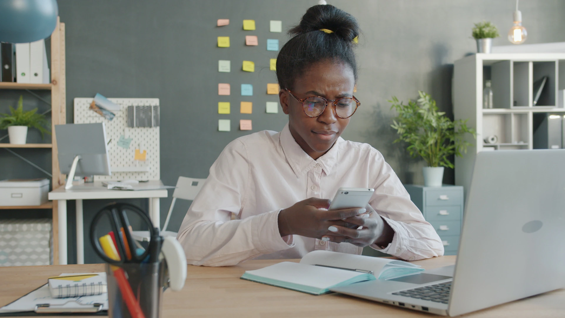Woman looking at phone at desk with laptop