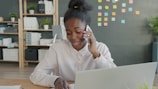Young woman talking on phone at office desk with laptop.